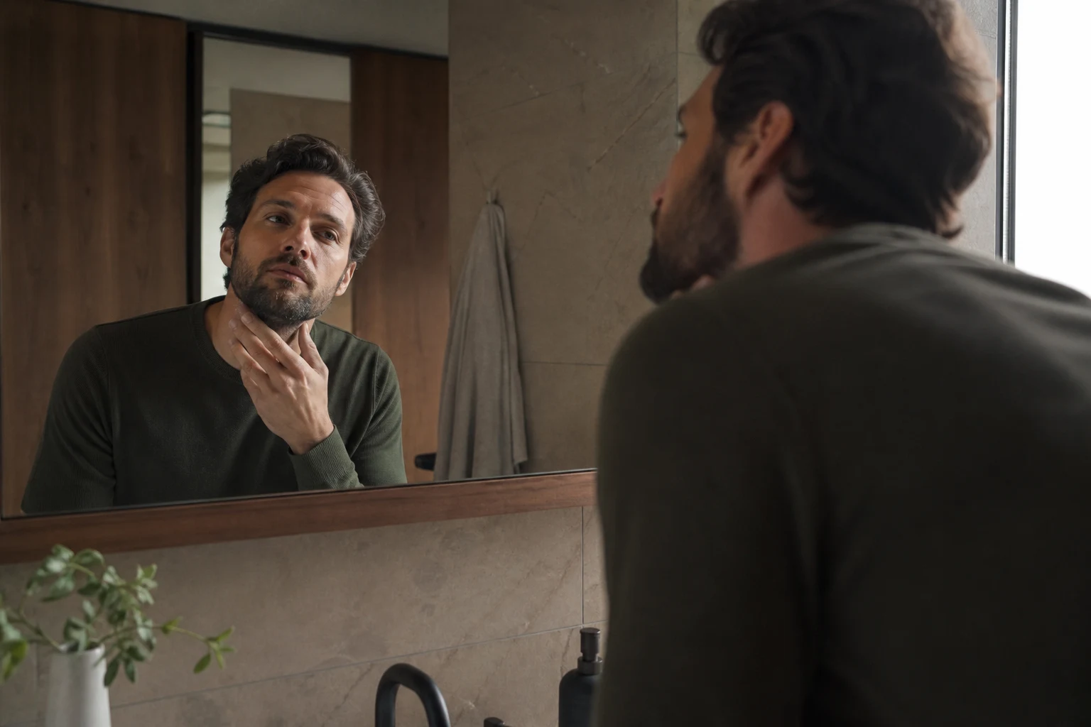 Adult studying his current hair and beard in a bathroom mirror